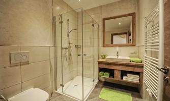 A modern bathroom with a walk-in shower and a wooden vanity. Green towels and a calming color palette create an inviting atmosphere.