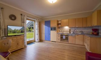 A modern kitchen with wooden cabinets and a large window overlooking the landscape. Bright and welcoming with a cozy living area.