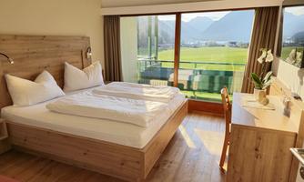 A modern room with a double bed and bright wooden interior. Large windows provide a view of the mountains and the landscape.