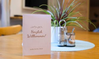 A welcome sign on a table with a plant and spice containers. The table is designed to be cozy and inviting.