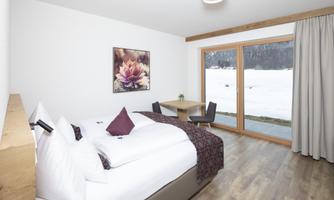A modern room with two beds and a table. Large windows offer a view of the snow-covered landscape outside.