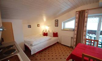 A cozy room with two beds and red pillows. A small table and a kitchen are also available.