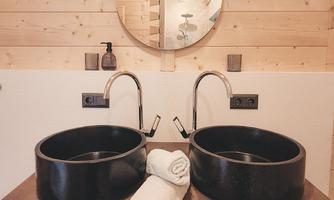 A modern bathroom with two round sinks and a large mirror. Below are a few towels.