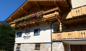 A beautiful apartment building with wooden cladding and a balcony. Flowers adorn the facade and give the building an inviting charm.