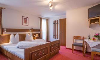 A cozy bedroom with a large bed and wooden decor. There is a table with flowers and a television on the wall.
