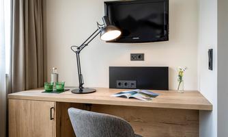 A modern office with a wooden desk, a monitor, and a desk lamp. There are water bottles and a small plant on the desk.