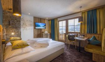 A cozy hotel room with a large double bed and modern furniture. The large windows offer a view of the mountains and plenty of daylight.