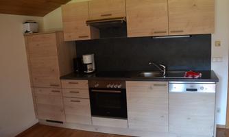 A modern kitchen with wooden cabinets and a stainless steel sink. It includes a stove, a refrigerator, and a coffee machine.