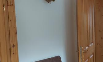 A cozy room with a wooden sofa and an open door. A stuffed eagle hangs on the wall.