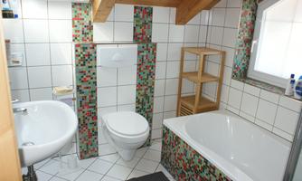 A modern bathroom with colorful mosaic tiles. It includes a sink, a toilet, and a bathtub.