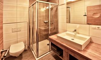 A modern bathroom with a shower cabin and a sink on a wooden vanity. The walls are brightly tiled, and there is bright lighting.