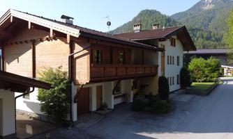 A traditional wooden house with a balcony and a beautiful garden landscape. In the background, green mountains can be seen.