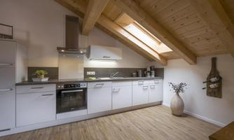 A modern kitchen with a wooden ceiling and large windows. The room is bright and friendly, with contemporary furnishings.