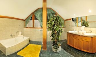 A modern bathroom with a bathtub and a large mirror. A plant stands next to the sink, and the floor is fitted with dark tiles.