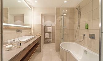 A modern bathroom with a bathtub and a shower. There is a large mirror and an elegant wooden shelf.