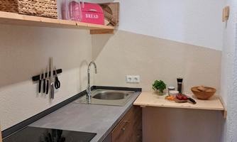 A modern kitchen with a stainless steel sink and a cooktop. Fresh vegetables and a bowl can be seen on the countertop.