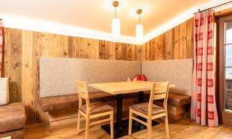 A cozy dining area with wooden paneling and modern lamps. The table is surrounded by comfortable benches, ideal for social gatherings.