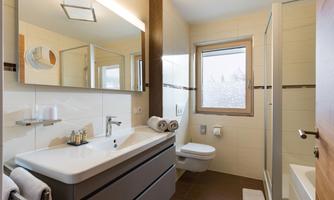 A modern bathroom with a large mirror and an elegant sink. The large tiles and natural light create a bright, inviting atmosphere.