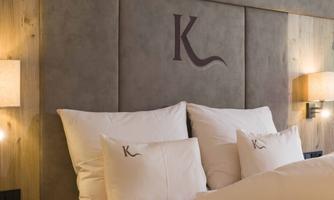 A cozy bedroom with an elegant headboard and white pillows. Soft lighting creates a relaxed atmosphere.