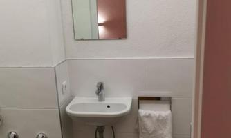 A modern bathroom with a small sink and a mirror. A towel hangs on the wall and a garbage can stands on the floor.