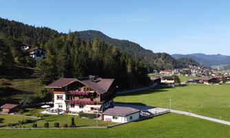 A picturesque landscape with a large house and green meadows. In the background, forests and mountains can be seen.