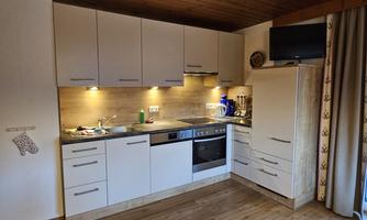A modern kitchen with white cabinets and wooden details. There is a stove, a refrigerator, and kitchen utensils.