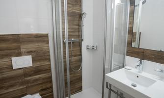 A modern bathroom with a shower and a sink unit. The walls are styled in light and dark wood tones.