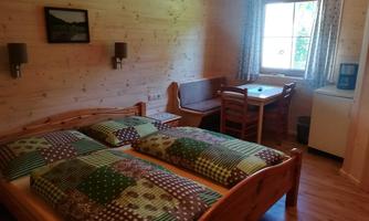 A cozy room with a double bed and wooden paneling. There is also a small dining area and a window with a view outside.