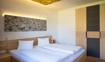 A modern bedroom with a large double bed and two pillows. The walls are bright and there are wooden surfaces that create a pleasant atmosphere.
