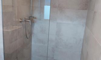 A modern shower with a glass partition and trendy tiles. The surroundings are bright and clean.