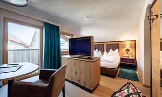 A cozy room with a large bed, a television, and a small table. The windows offer a view of the landscape.