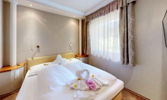 A cozy bedroom with a double bed and soft lighting. The windows are adorned with curtains and fresh flowers are lying on the bed.