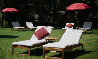 Elegant loungers on a green meadow, surrounded by red sun umbrellas. The ideal place to relax outdoors.