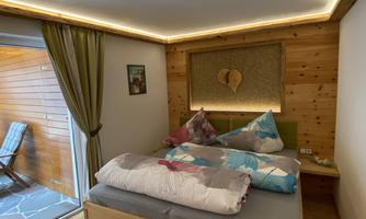A modern bedroom with wooden walls and a double bed. The room has a cozy atmosphere and access to a terrace.