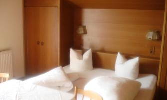 A cozy bedroom with a double bed and white pillows. The walls are made of wood and the room has a warm atmosphere.