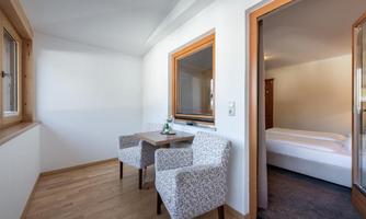 A bright, modern room with two chairs and a table. In the background, a bedroom with a bed can be seen.