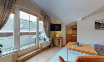 A cozy living room with windows that offer a view of the mountains. The decor is modern and inviting, featuring a wooden table and a couch.