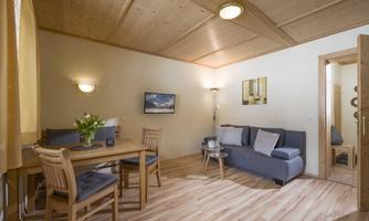 A modern living room with wooden ceilings and a cozy sofa. A table with chairs and a blooming plant complete the space.