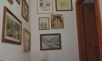 A narrow hallway with a wooden frame and various pictures on the wall. In the corner stands a statue depicting a mother with her child.