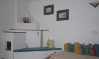 A cozy room with a couch and colorful cushions. Pictures hang on the wall and there is a small windowsill.