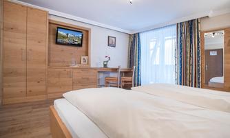 A cozy hotel room with wooden furniture and two beds. A television is mounted on the wall, and there is a window with curtains.