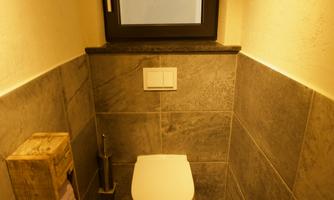 A small bathroom with a modern toilet. The walls are covered with gray tiles and a window provides natural light.