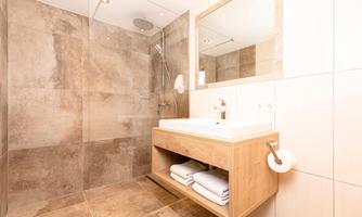 A modern bathroom with a glass shower and a wooden sink. Soft towels are neatly stored.