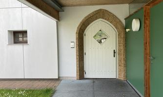 An entrance with a white Gothic-style door and an oval window opening. The surroundings depict a clear wall, a green wall section, and a wooden porch.