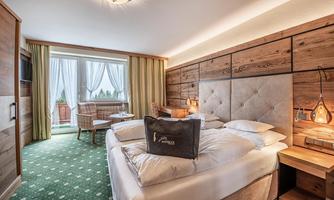 A cozy hotel room with a double bed and a balcony. The room is decorated with wood decor and a green carpet.