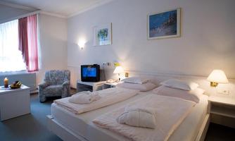 A cozy hotel room with two beds and a television. The room has large windows and a color palette in soft tones.