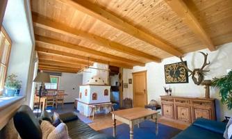 A cozy living room with a wooden ceiling and a large table. A fireplace is situated on one wall, and decorative elements create an inviting atmosphere.