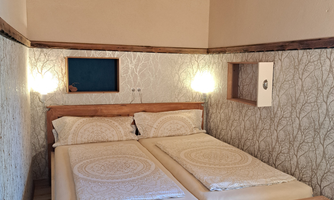 A cozy bedroom with two beds and soft lighting. The walls are decorated with a stylish, natural pattern.