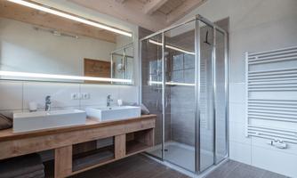 A modern bathroom with double sinks and a glass shower. The bright furnishings and wooden paneling create a cozy atmosphere.