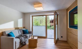 A modern living room with a comfortable couch and two blue cushions. Large windows offer a view of greenery and plenty of daylight.
